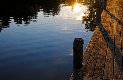 Romantic evening at the lake. The last rays of sun are reflected in the water, and the evening light gently bathes the jetty in warm colours.