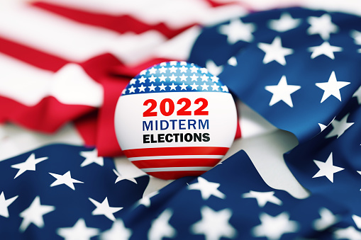 2022 Midterm Elections written badge sitting over rippled American flag. Great use for election and voting concepts. 2022 US Midterm Election concept. High angle view.