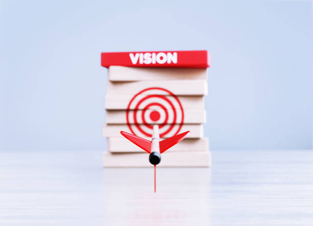 Arrow Hitting Red Bull's Eye Target And Vision Written Wood Blocks in Front a Defocused Background