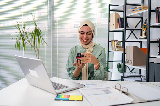 Businesswoman wearing hijab using desktop PC in office. Female professional is working at computer desk. She is wearing traditional clothing.