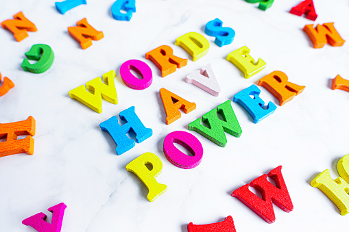 Multicolored wooden letter characters arranged into the wording WORDS HAVE POWER on gray. Creative education concept.
