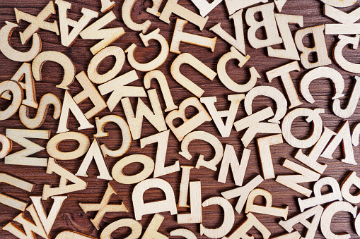 Abstract background made from scattered wooden letter characters on a dark wooden table.