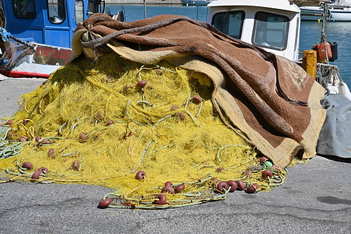 Heraklion, Greece - 22 09 2022: Close view on yellow fishing net with red-brown floats piled on pavement in port of Heraklion ready for loading on fishing boat moored nearby. Net is covered by carpet.