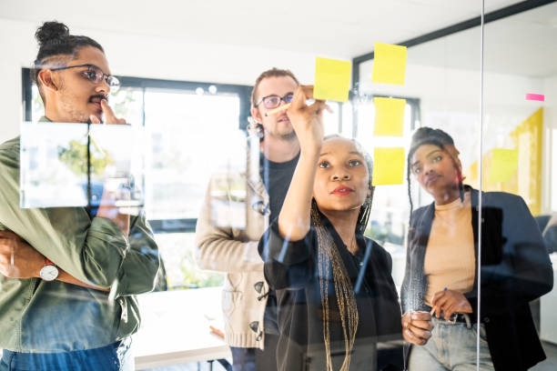 istock African businesswoman using sticky notes on glass board and discussing project with team 1430093015
