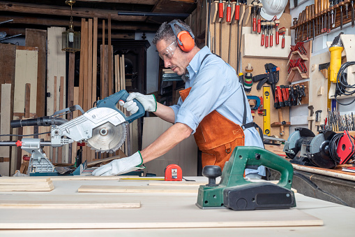 CARPENTER IN THE WORKSHOP WORKING WOOD USING A MITER SAW. DIY CONCEPT.