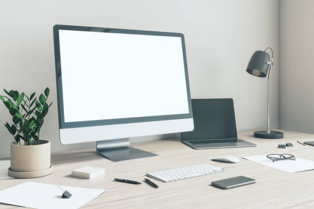 istock Side view on blank white modern computer monitor with copyspace in home office with light wall, dark laptop and lamp, flowerpot and smartphone on wooden table. 3D rendering, mockup 1430102363