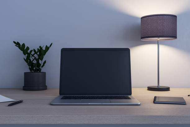 istock Front view on blank black modern laptop screen with place for your logo or text on wooden table with flowerpot, switched on lamp and notebook. 3D rendering, mock up 1430102516