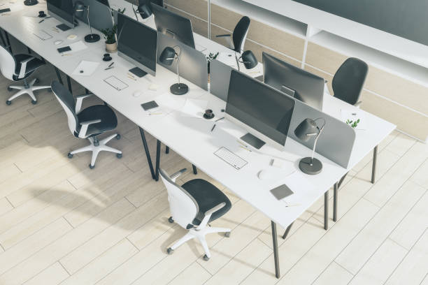 istock Top view on minimalistic style raw of workplaces with modern computers, white tables and light wooden floor in sunny coworking office. 3D rendering 1430102520