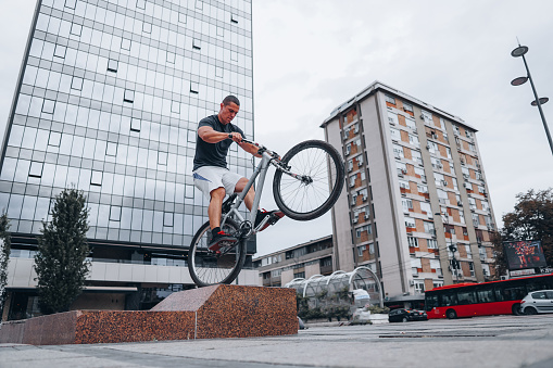 Stunt man riding a bike on one wheel in an urban area, city center