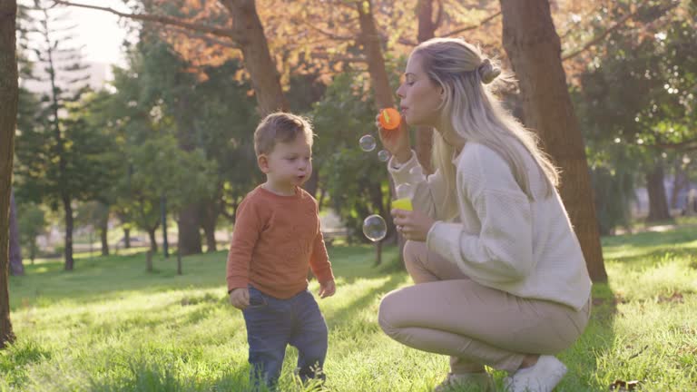 Happy family, mother and child with bubbles in park, having fun in autumn. Childhood, entertainment and the joy of innocence. Smiling young parent bonding with son in nature with trees.