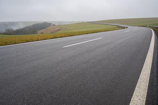 Close up of a long asphalt road in the countryside on a wet and foggy morning in December