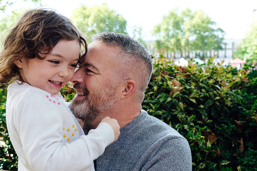 Bearded father with his little daughter in his arms in the park hugging and kissing.