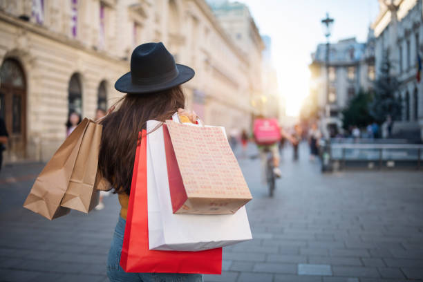 vista posteriore della donna con un cappello che cammina per la strada della città e trasporta borse della spesa. - solo ragazze foto e immagini stock