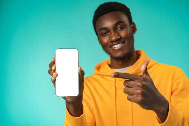 istock Smiling casual black man pointing at blank white cell phone screen in studio 1430110197