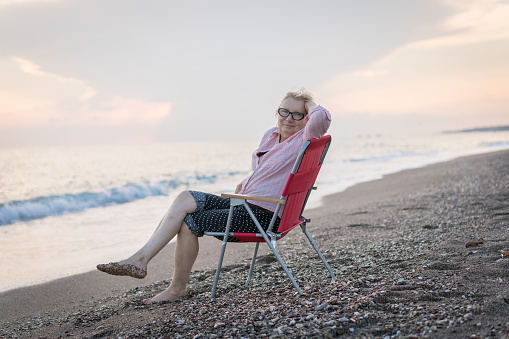 Senior woman sitting on chair and looking at camera by sunset
