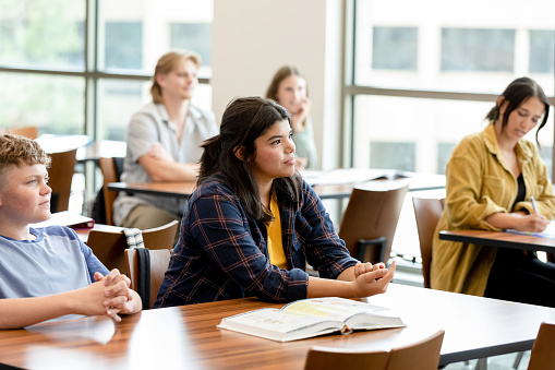 The college students take notes as they listen to their professor give his lecture.