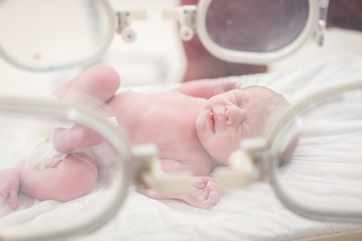 A newborn baby in an incubator in a hospital ward.