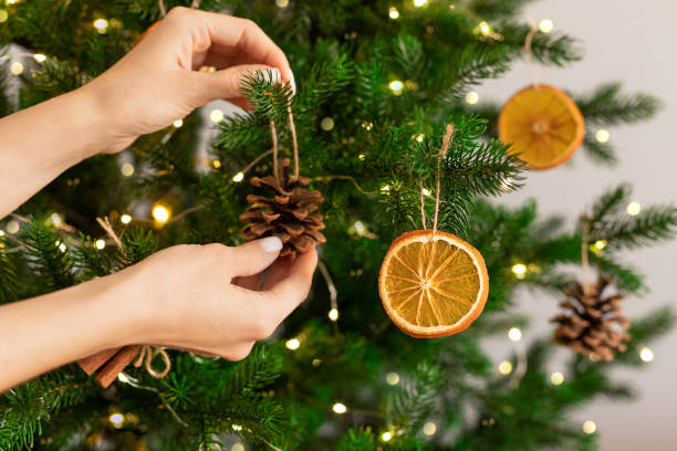 mains féminines accrochant une décoration faite à la main sur un arbre de noël. - pomme de pin photos et images de collection