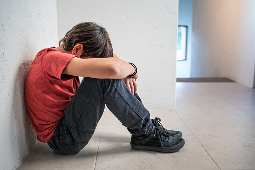 depressed, sad, upset boy sitting on floor with head down