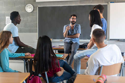 Joven maestra hablando con estudiantes adolescentes sentados en círculo en la escuela photo