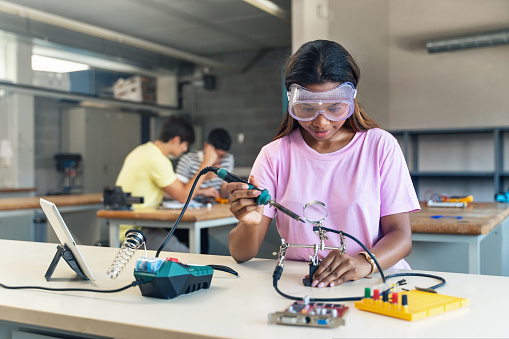 Adolescente afroamericano de secundaria Estudiante con gafas protectoras soldando circuito electrónico en el taller de ciencia tecnología - Innovación Digital en Educación photo