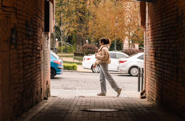 Photo of A woman walks along a city street, a view from the alley, a casual passer-by.