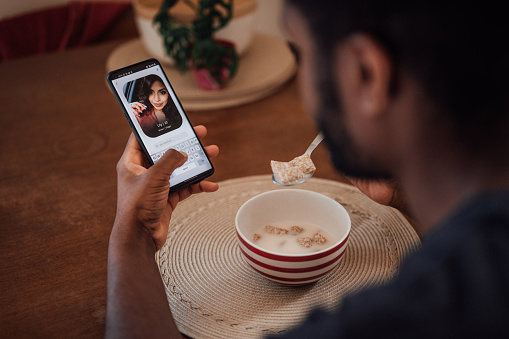 over the shoulder image of young man checking his phone while eating breakfast