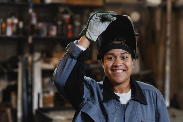 Woman Welding Metal In Workshop Closeup portrait of smiling female welder looking at camera in industrial factory, copy space manufacturing occupation stock pictures, royalty-free photos & images