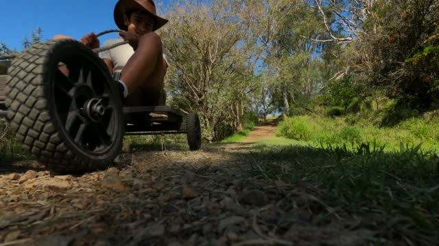 Boy on old homemade go kart on country track or drives close to camera at low angle view