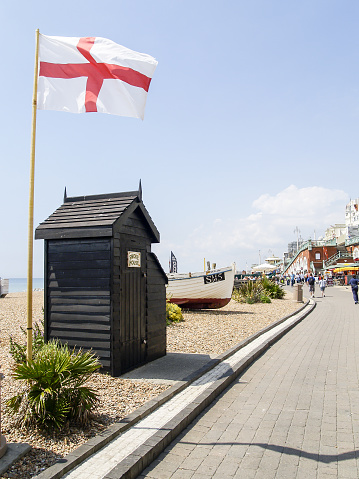 Brighton Beach United Kingdom - June 16 2009; Small dark brown building with Smoke House on door sign and flag of England beside path leading along beach.