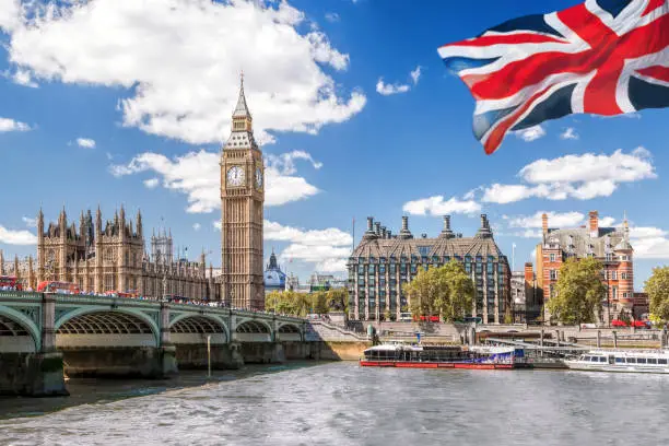 Photo of Big Ben with bridge over Thames and flag of England against blue sky in London, England, UK