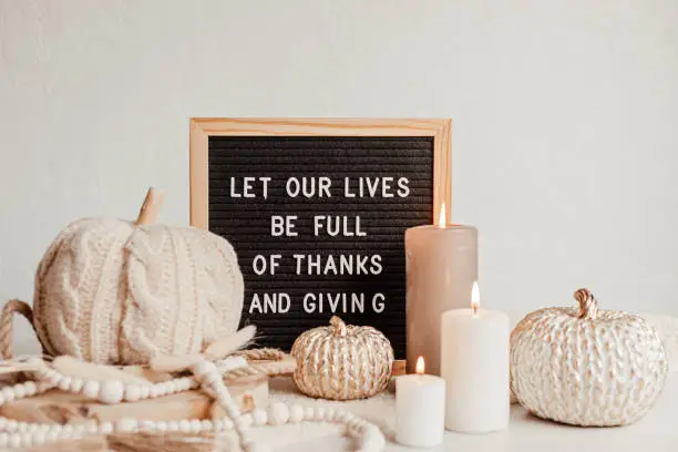 Photo of Felt letter board and text let our lives be full of thanks and giving. Autumn table decoration. Interior decor for thanksgiving and fall holidays with handmade pumpkins and candles