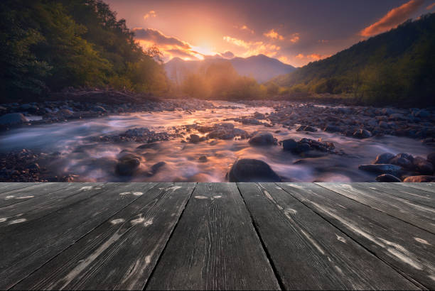 Beautiful sunset over fast flowing mountain river with empty wooden batten bridge. Natural template landscape stock photo
