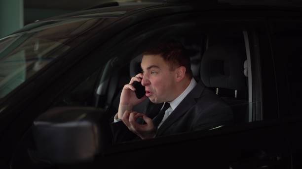 The young boss swears and shouts on the phone while sitting in the car in the parking lot. Angry businessman speaks on the phone. The young boss swears and shouts on the phone while sitting in the car in the parking lot. Angry businessman speaks on the phone. 4k speaking with forked tongue stock pictures, royalty-free photos & images