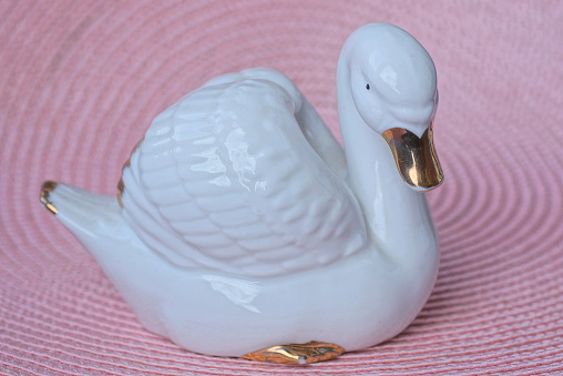 one small figurine of a white ceramic swan stands on a pink table