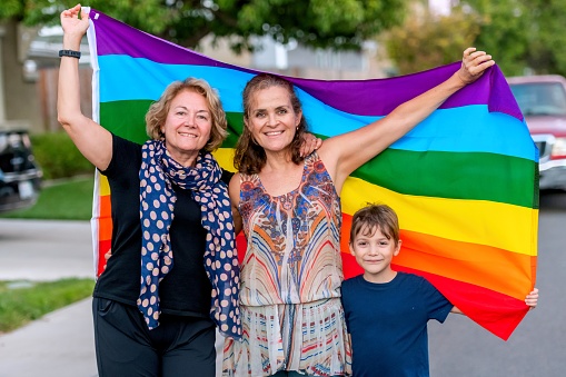 Mature lesbian couple posing with their son holding a rainbow flag
