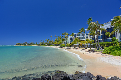 Oceanfront condos with palm trees on an empty sandy beach along the quiet and uncrowded Kahala Beach area in Honolulu on Oahu, Hawaii.