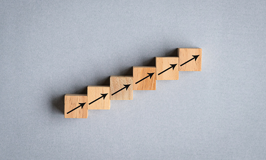 Arrows on wood cubes arranged as step stair going up. Growth or uptrend concept.