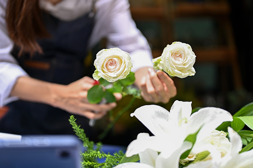 Professional female florist or flower shop worker arranging a beautiful bouquet, making a white roses bouquet for her customer. cropped and close-up image