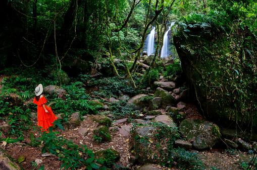 Beautiful woman in red dress in front of the Sapan Waterfall, Khun Nan National Park, Boklua District, Nan Province, Thailand.
