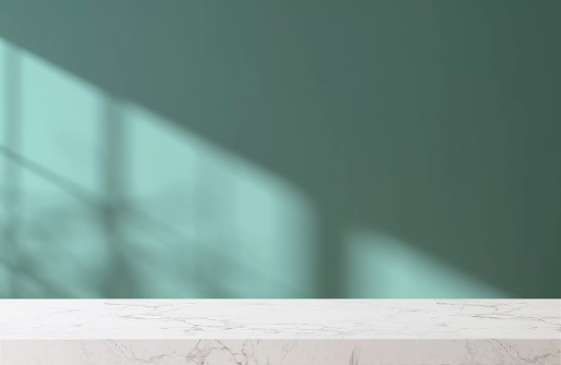 White marble tabletop or countertop in modern and minimal turquoise green blue wall room with sunlight and tree shadow from window at home