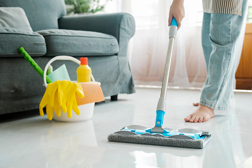 Young woman in casual clothes cleaning wasing floor using mop with cleaning solution in living room at home. Woman doing housechores at home. Housekeeping concept.