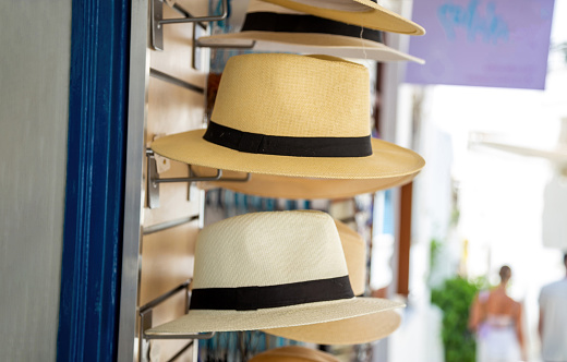 Straw handmade multicolor hats on outdoors stand, at Greek island souvenir street shop. Blur pedestrians, headwear protection from summer sun.