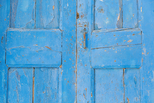 Wooden closed door background, texture. Blue empty peeled shabby board planks with rusty metal handle, keyhole. Traditional Greek island construction.