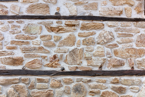 Old grey stone wall made of many rough natural stones of assorted sizes.