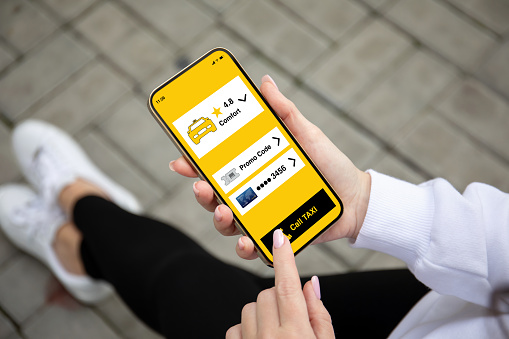 female hand holding golden phone with taxi call application on the screen street background
