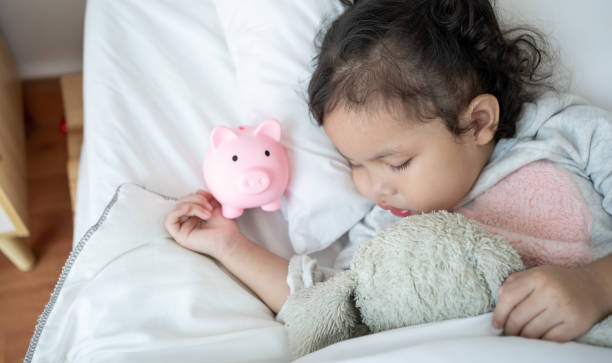 caucasian cute female child sleeping on a piggybank on bedroom.baby taking a nap and a piggy bank.childcare cost life insurance. - junior high fotos imagens e fotografias de stock