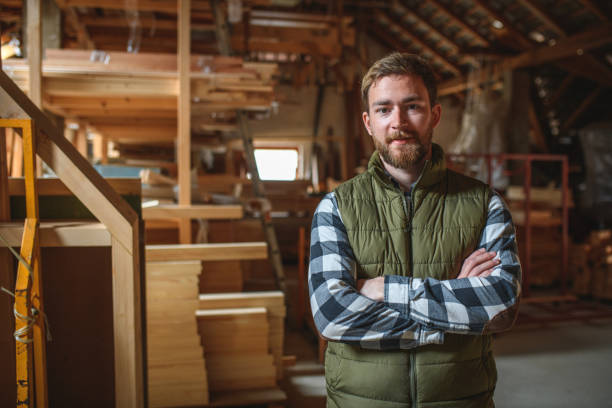 Caucasian Young Adult Carpenter In A Workshop Portrait of a Caucasian young adult carpenter standing in a workshop with his hands folded looking at camera. carpenter portrait stock pictures, royalty-free photos & images