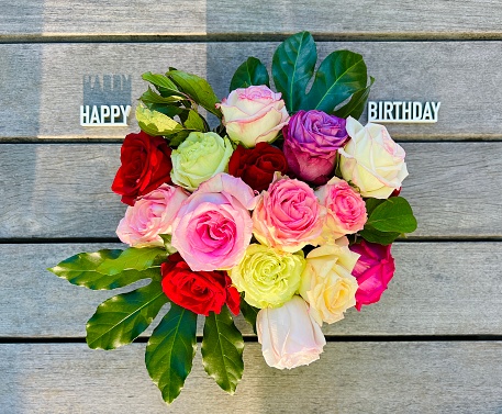 Bunch of multi colored roses on wooden planks, happy birthday lying on planks