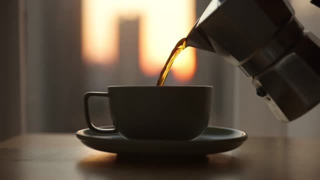 Pouring freshly brewed black coffee in a cup at sunrise